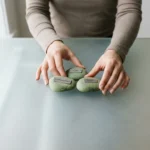 A person's hands thoughtfully arranging three green stones labeled 'CPI', 'Unemployment', and 'GDP' on a frosted glass surface, representing economic indicators.