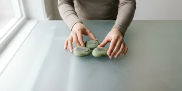 A person's hands thoughtfully arranging three green stones labeled 'CPI', 'Unemployment', and 'GDP' on a frosted glass surface, representing economic indicators.