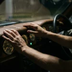 A person's hands on a vintage car dashboard with analog gauges, symbolizing economic indicators for financial navigation.