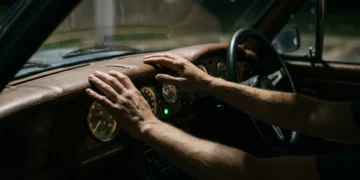 A person's hands on a vintage car dashboard with analog gauges, symbolizing economic indicators for financial navigation.